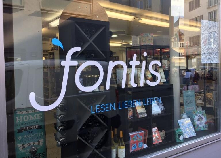 Die Fontis-Buchhandlung in Aarau präsentiert sich mit dem Wort „Fontis“ und dem Slogan „LESEN. LIEBEN. LEBEN“. Bücher, Weine und andere Artikel sind liebevoll arrangiert und durch die Glasscheibe sichtbar.