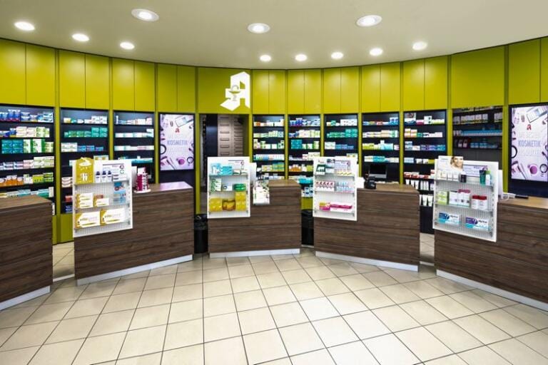 Moderne Apotheke Rheinfeld mit mehreren Holztheken, Regalen voller Gesundheitsprodukte und heller Beleuchtung. Grüne und schwarze Wandpaneele säumen die Regale im Hintergrund und sorgen für einen modernen Look.