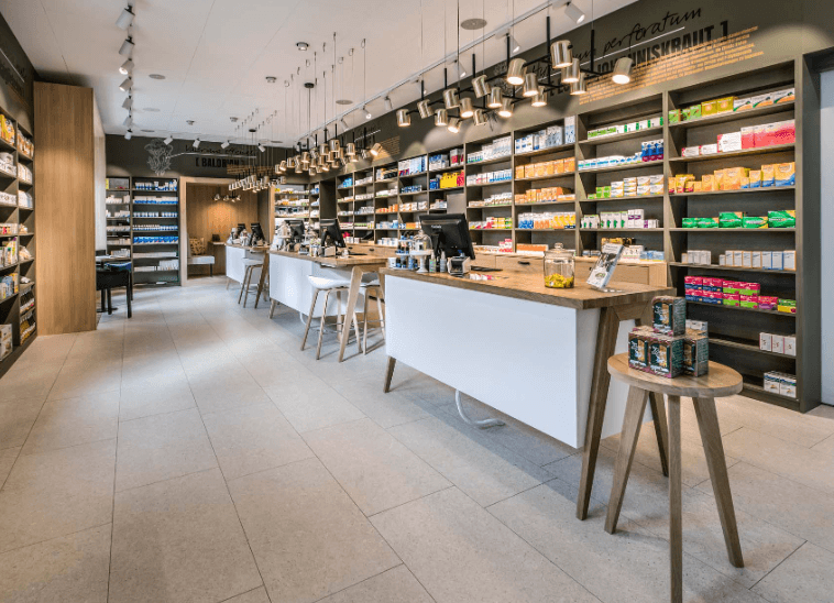 Eine moderne Apothekeneinrichtung bei TopPharm mit gut beleuchteten Regalen voller Gesundheitsprodukte, zwei weißen Theken mit Computern und Holzakzenten im gesamten Raum.