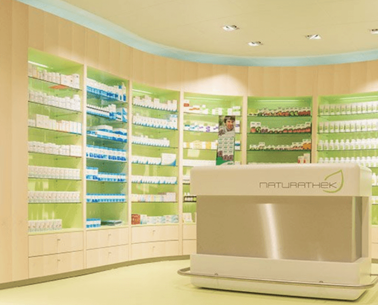 Ein hell erleuchteter Apothekeninnenraum in Langnau mit geschwungenen Regalen, gefüllt mit verschiedenen Schachteln und Flaschen. Im Vordergrund steht ein Tresen mit der Aufschrift „NATURATHEK“, der in einem beruhigenden Hellgrün- und Creme-Farbschema gehalten ist.
