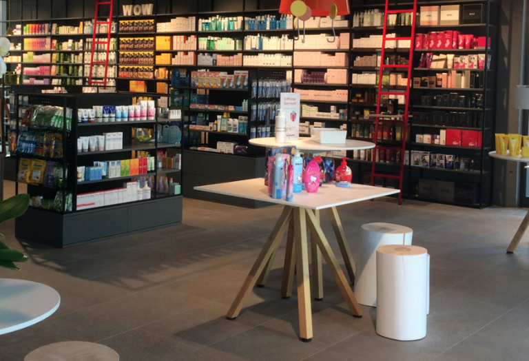 Eine moderne Drogerie mit Regalen voller Hautpflege- und Schönheitsprodukte. Im Vordergrund präsentieren Tische Geschenksets und andere Artikel. Der Raum ist hell und übersichtlich, mit Hockern und übersichtlich angeordneten Waren.