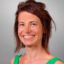 Bianca Iten, mit kurzen braunen Haaren und einem breiten Lächeln, trägt ein ärmelloses grünes Top. Der Hintergrund ist schlicht und neutral grau – ein Ausdruck der einladenden Atmosphäre der Praxis am Aabach.