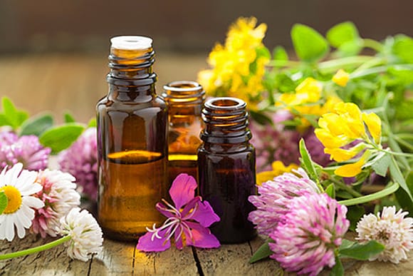 Drei kleine Bernsteinglasflaschen, zwei offen und eine verschlossen, von der Marvitalis GmbH, sind von bunten Wildblumen umgeben, darunter Gänseblümchen, Klee und gelbe Blüten, alles auf einer rustikalen Holzoberfläche arrangiert.