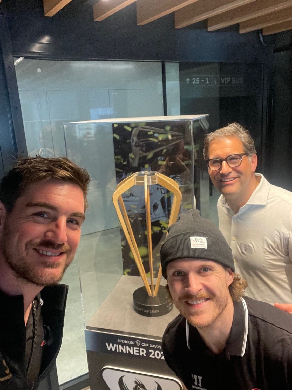 Drei lächelnde Männer posieren für ein Selfie vor einer Vitrine mit der Trophäe „WINNER 2024“ unter dem Titel „SPIENGLE CUP DAVOS“ und feiern damit den Schweizer Eishockeysport. Im Hintergrund ist ein VIP SUD-Schild zu sehen.
