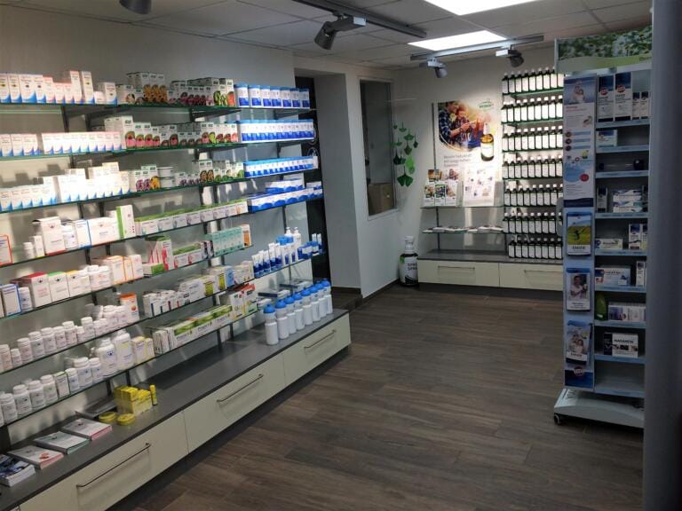 Ein sauberer, gut beleuchteter Innenraum der Drogerie Grindelwald mit Holzböden und übersichtlichen Regalen voller Gesundheitsprodukte. Poster und Broschüren an den Wänden und in den Auslagen sorgen für eine einladende Atmosphäre.