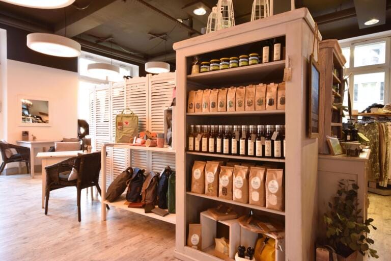 Ein gemütliches Ladeninterieur mit Regalen voller verpackter Waren, Flaschen und Gläsern. Im Hintergrund präsentiert HARMony Tische, Stühle und Accessoires, alles unter warmer, moderner Deckenbeleuchtung.