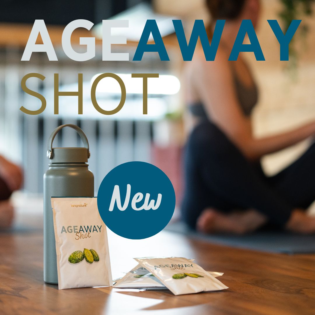 Päckchen mit der Aufschrift „AgeAway Shot“ und eine Wasserflasche liegen auf einer Yogamatte. Im Hintergrund sitzt eine Person in Trainingskleidung im Schneidersitz. In großen Buchstaben steht „AGEAWAY SHOT“, „Neu“ und „Longevity-Produkt“.